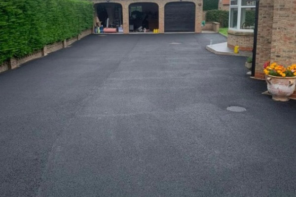 Clean and restored black tarmac driveway in front of a Yorkshire home, after pressure washing and sealing by Pro-Juvenate UK